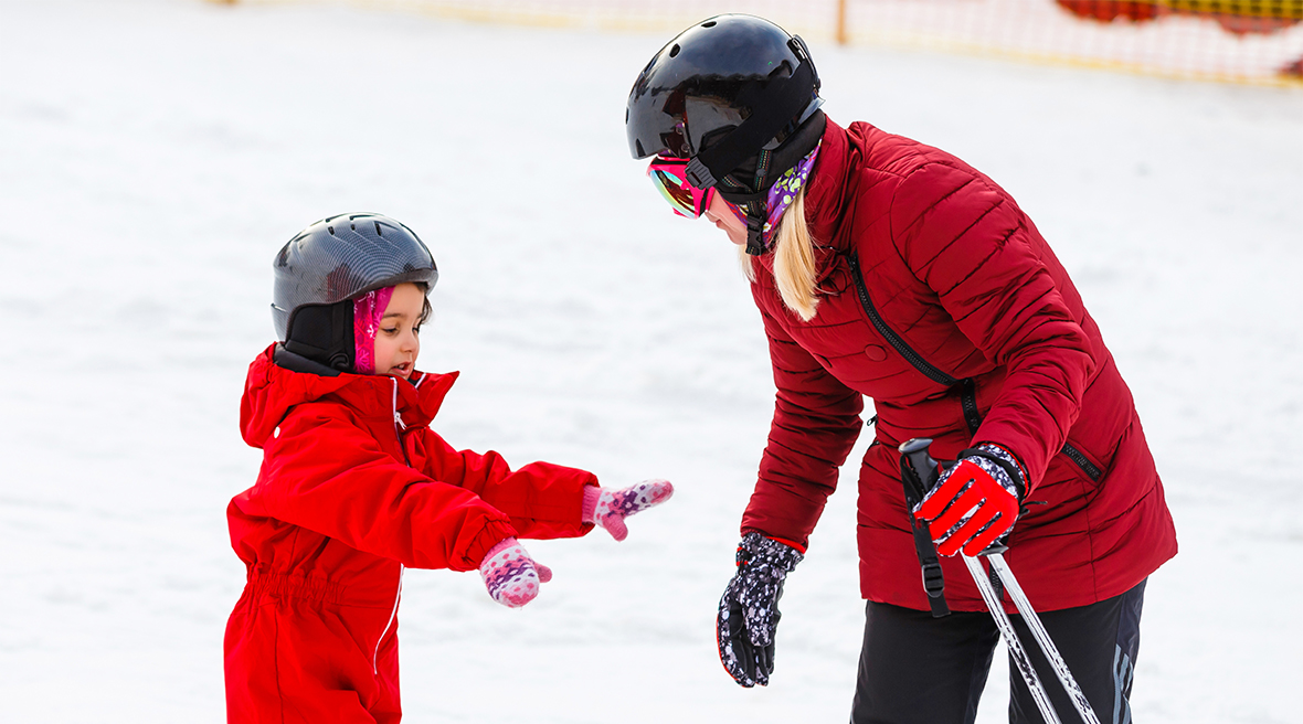 Little girl in a red ski suit snow learning to ski holding out her hands to a ski instructor